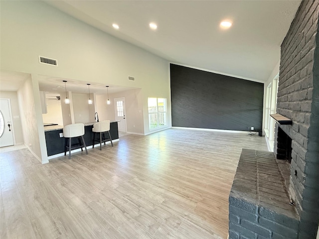 living room featuring a brick fireplace, high vaulted ceiling, sink, and light wood-type flooring