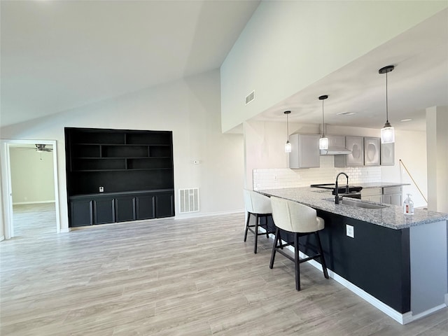 kitchen with lofted ceiling, kitchen peninsula, light hardwood / wood-style floors, and gray cabinetry