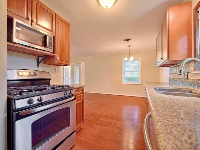 kitchen with decorative light fixtures, sink, light stone counters, light hardwood / wood-style floors, and stainless steel appliances