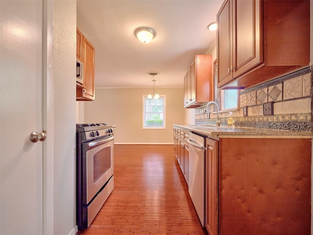 kitchen featuring sink, hanging light fixtures, appliances with stainless steel finishes, light hardwood / wood-style floors, and backsplash