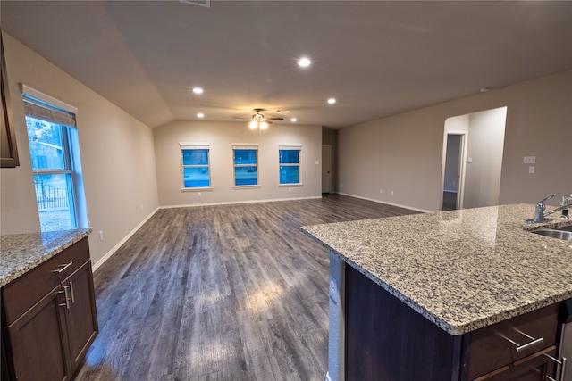 kitchen featuring sink, vaulted ceiling, dark hardwood / wood-style floors, an island with sink, and light stone countertops