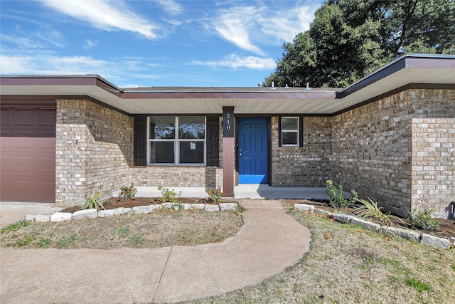 property entrance with covered porch, brick siding, and an attached garage