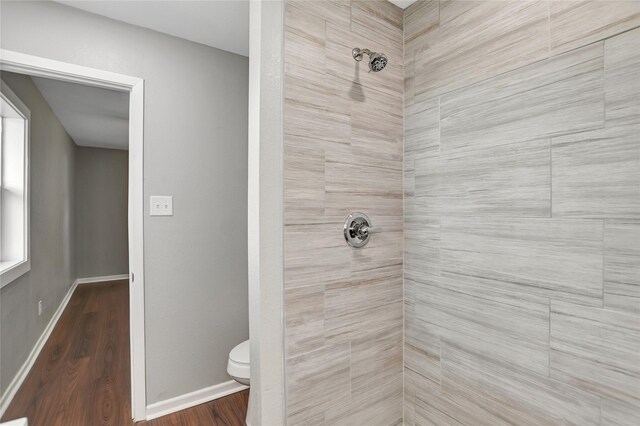 bathroom with tiled shower, toilet, and hardwood / wood-style floors