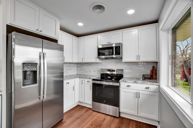 kitchen featuring white cabinetry, stainless steel appliances, light stone counters, decorative backsplash, and light wood-type flooring