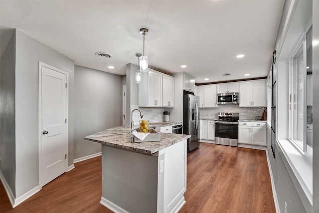 kitchen featuring white cabinetry, pendant lighting, stainless steel appliances, light stone countertops, and hardwood / wood-style floors