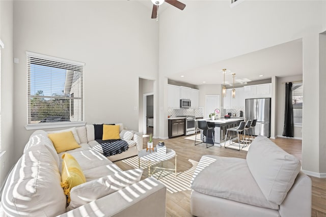 living room featuring light hardwood / wood-style floors, ceiling fan, and a high ceiling