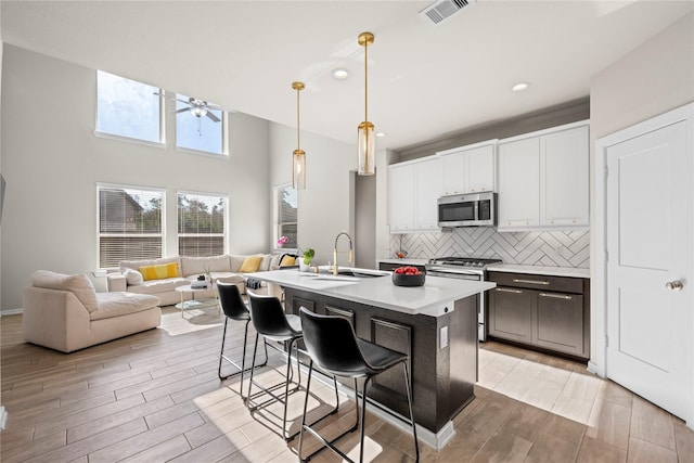 kitchen with sink, white cabinetry, hanging light fixtures, an island with sink, and stainless steel appliances