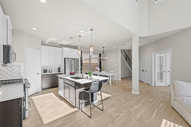 kitchen with white cabinetry, backsplash, stainless steel appliances, and a center island with sink