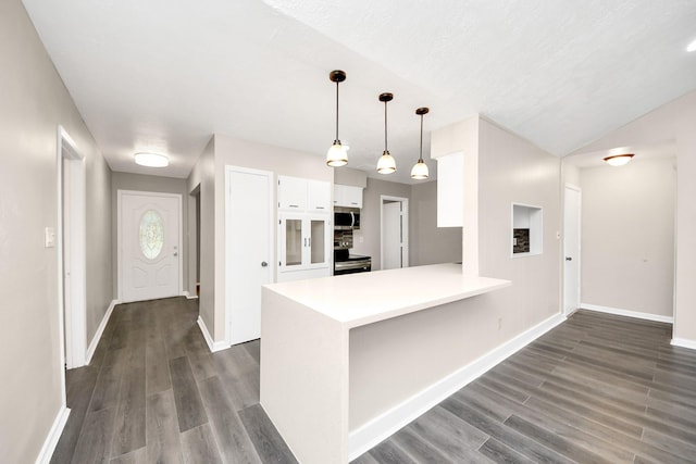 kitchen with appliances with stainless steel finishes, white cabinetry, hanging light fixtures, kitchen peninsula, and dark wood-type flooring