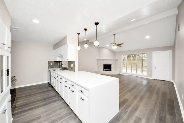 kitchen featuring sink, a fireplace, white cabinets, decorative backsplash, and vaulted ceiling