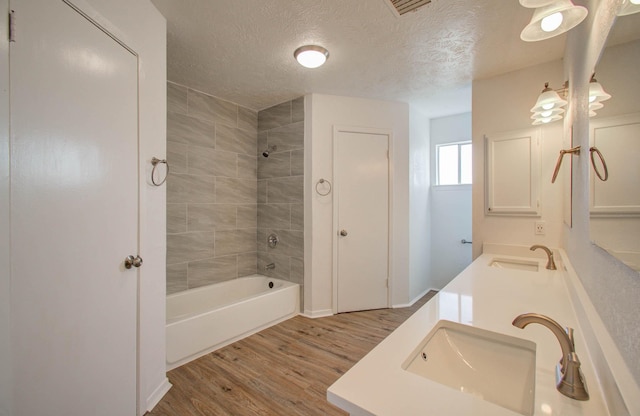 bathroom with tiled shower / bath, wood-type flooring, vanity, and a textured ceiling