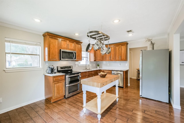 kitchen featuring sink, tasteful backsplash, light hardwood / wood-style flooring, ornamental molding, and stainless steel appliances