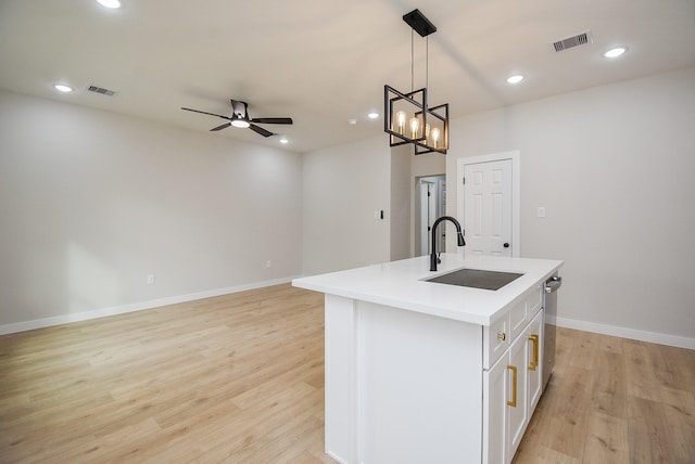 kitchen featuring ceiling fan with notable chandelier, an island with sink, sink, white cabinets, and hanging light fixtures