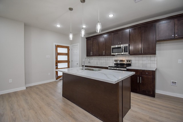 kitchen featuring sink, light stone counters, hanging light fixtures, appliances with stainless steel finishes, and an island with sink