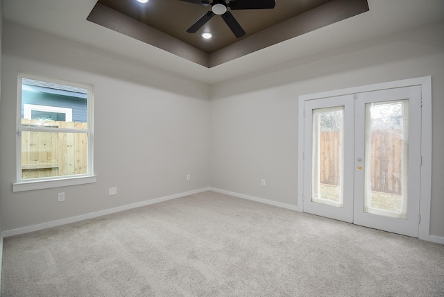 empty room featuring a raised ceiling, light carpet, ceiling fan, and french doors