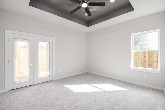 carpeted empty room featuring a raised ceiling, ceiling fan, and french doors