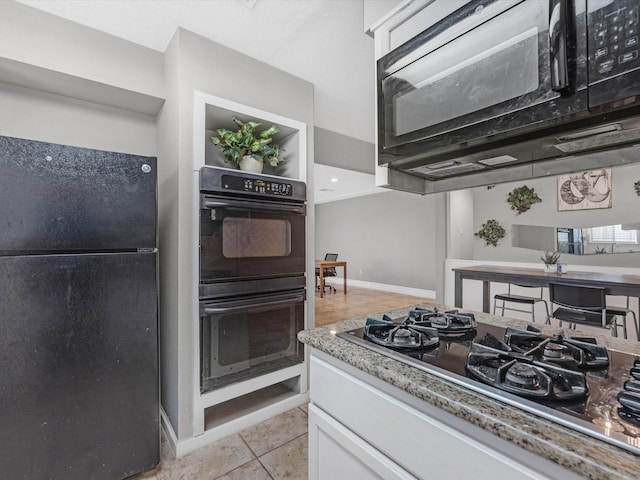 kitchen with light tile patterned floors, white cabinets, light stone counters, and black appliances