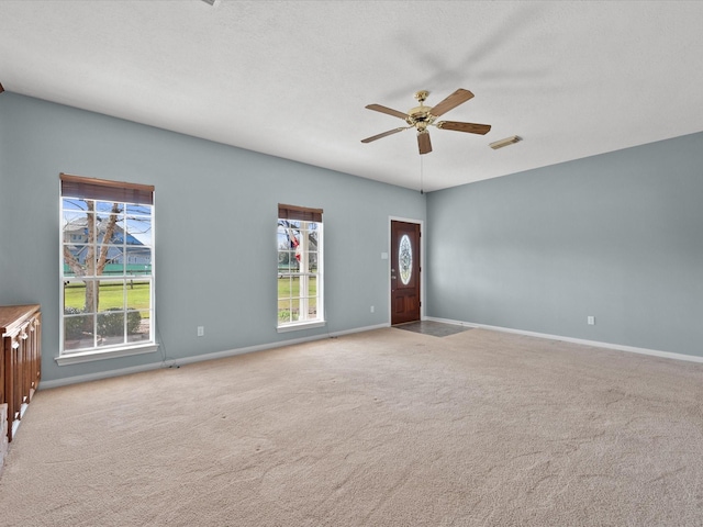 unfurnished living room with light carpet, a ceiling fan, visible vents, and a wealth of natural light