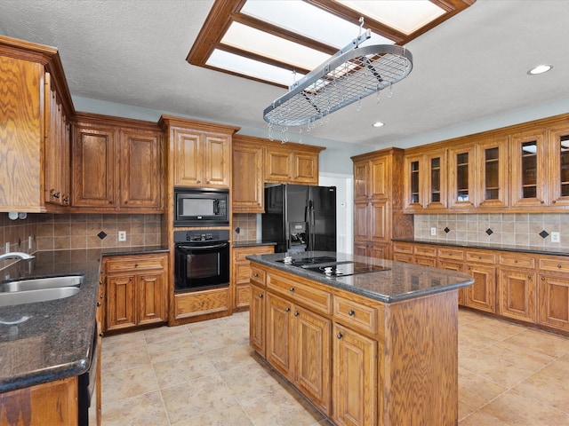 kitchen featuring brown cabinets, glass insert cabinets, a sink, a kitchen island, and black appliances