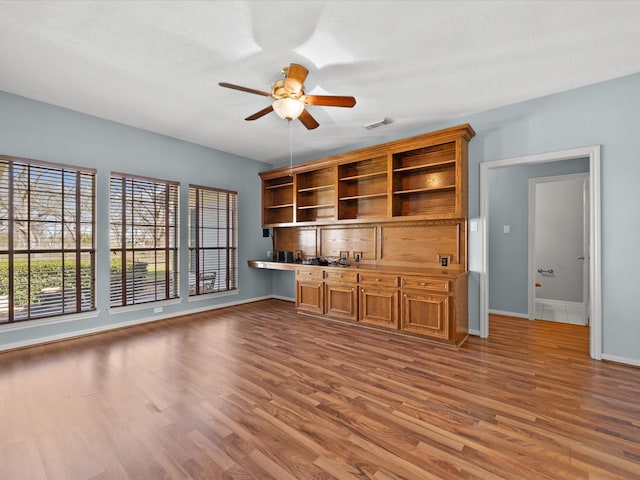 unfurnished living room featuring ceiling fan, built in desk, wood finished floors, and visible vents