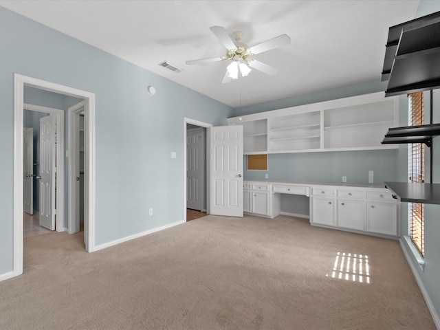 interior space with light colored carpet, visible vents, built in desk, and baseboards