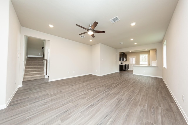 unfurnished living room featuring visible vents, baseboards, light wood-style flooring, stairway, and recessed lighting