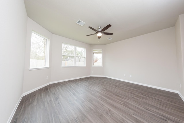 unfurnished room with a ceiling fan, dark wood-style flooring, visible vents, and baseboards