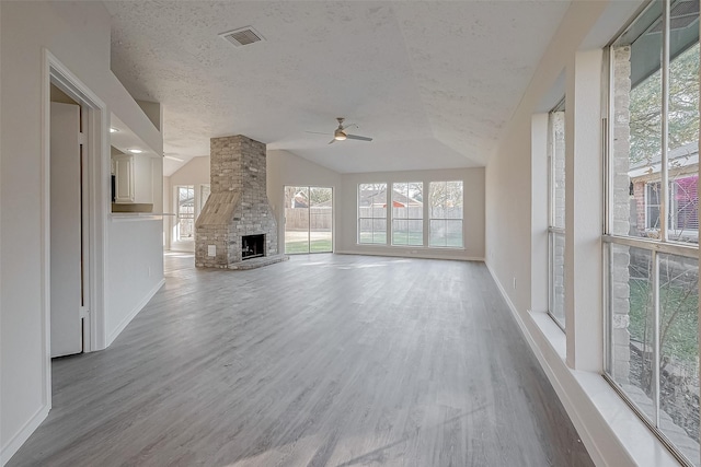 unfurnished living room featuring vaulted ceiling, a fireplace, hardwood / wood-style flooring, ceiling fan, and a textured ceiling