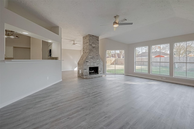 unfurnished living room with hardwood / wood-style flooring, ceiling fan, a fireplace, a textured ceiling, and vaulted ceiling