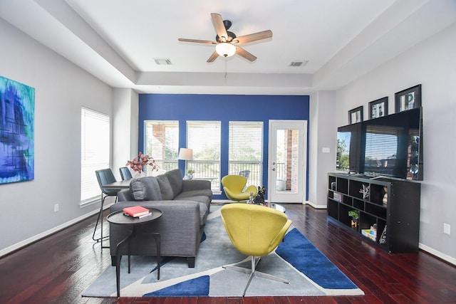 living room featuring dark wood-type flooring, a raised ceiling, and ceiling fan