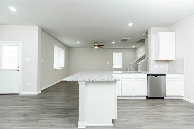 kitchen featuring tasteful backsplash, white cabinetry, stainless steel dishwasher, light stone counters, and light hardwood / wood-style flooring