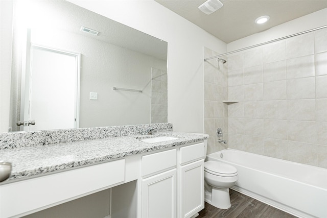 full bathroom featuring hardwood / wood-style flooring, vanity, tiled shower / bath combo, and toilet