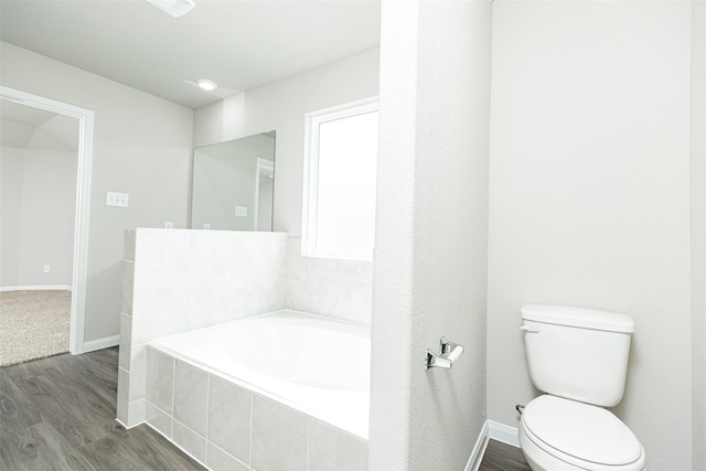 bathroom featuring a relaxing tiled tub, hardwood / wood-style flooring, and toilet