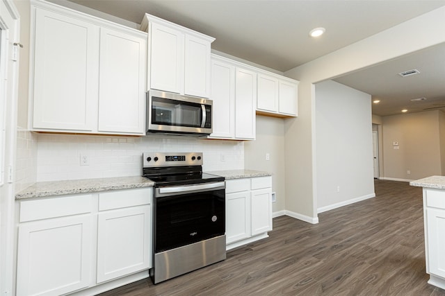 kitchen with backsplash, stainless steel appliances, light stone counters, white cabinets, and dark hardwood / wood-style flooring