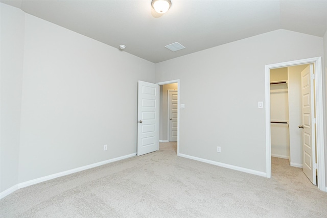 unfurnished bedroom with lofted ceiling, a walk in closet, and light colored carpet