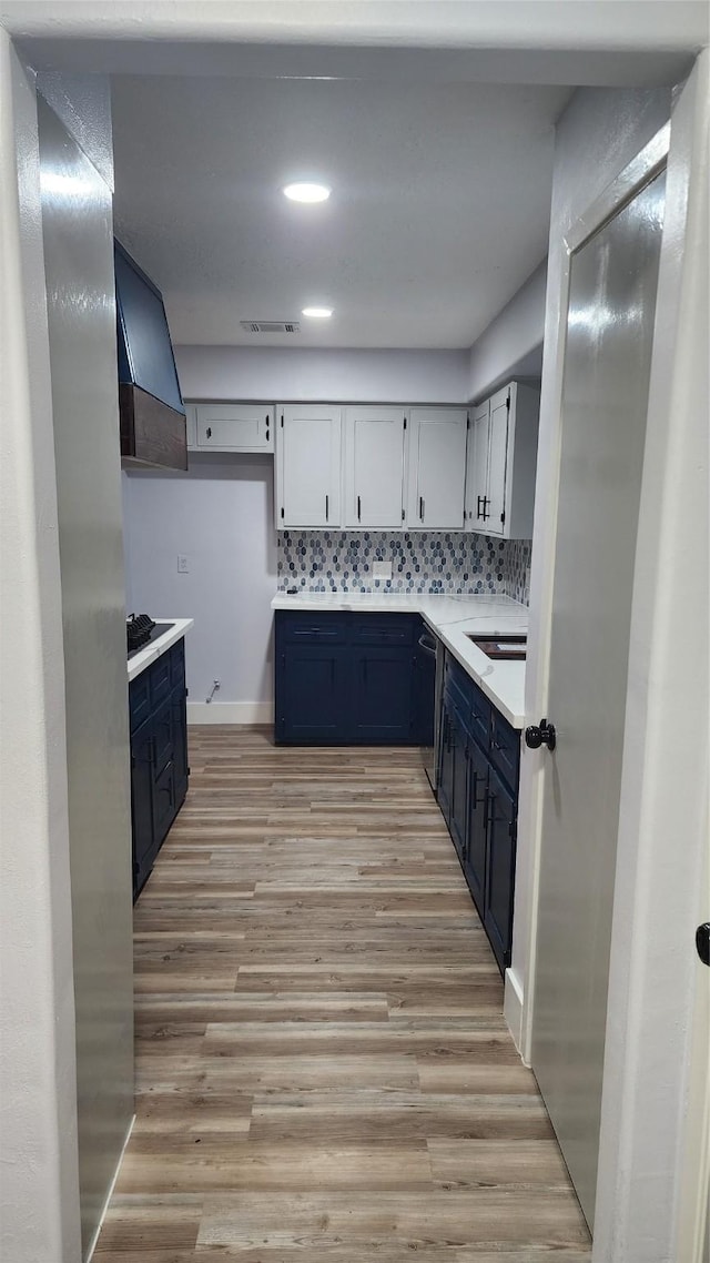 kitchen featuring sink, blue cabinetry, premium range hood, tasteful backsplash, and light wood-type flooring