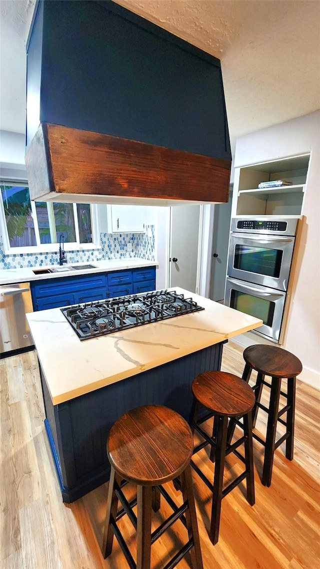 kitchen with sink, appliances with stainless steel finishes, a kitchen bar, blue cabinets, and light wood-type flooring