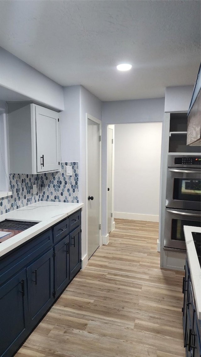 kitchen featuring blue cabinetry, stainless steel double oven, decorative backsplash, and light wood-type flooring