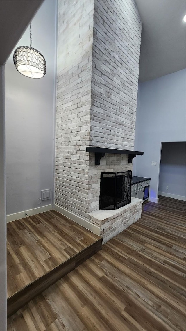 unfurnished living room featuring a brick fireplace and dark wood-type flooring