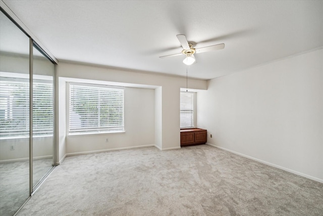 unfurnished bedroom with multiple windows, light colored carpet, ceiling fan, and a closet