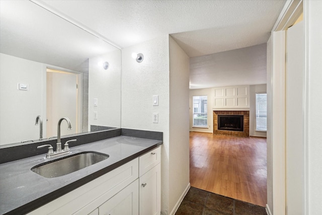 kitchen featuring white cabinetry, sink, a textured ceiling, and a brick fireplace