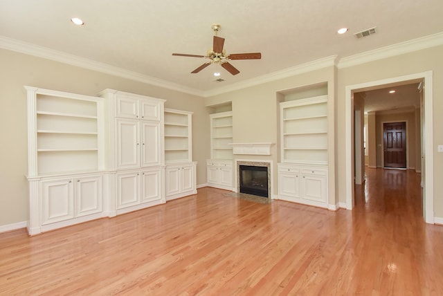 unfurnished living room featuring built in features, ceiling fan, a fireplace, ornamental molding, and light wood-type flooring