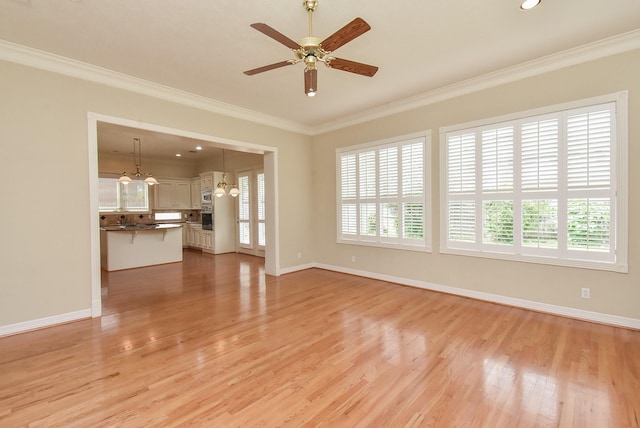 unfurnished living room featuring ornamental molding, ceiling fan with notable chandelier, and light wood-type flooring