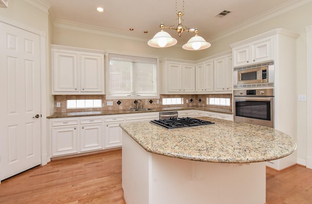 kitchen with appliances with stainless steel finishes, white cabinetry, sink, hanging light fixtures, and a center island