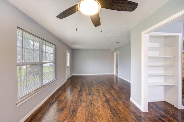 empty room featuring ceiling fan, a textured ceiling, built in features, baseboards, and dark wood-style floors