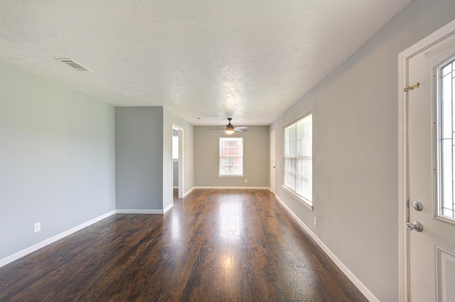 unfurnished room with ceiling fan, a textured ceiling, visible vents, baseboards, and dark wood finished floors