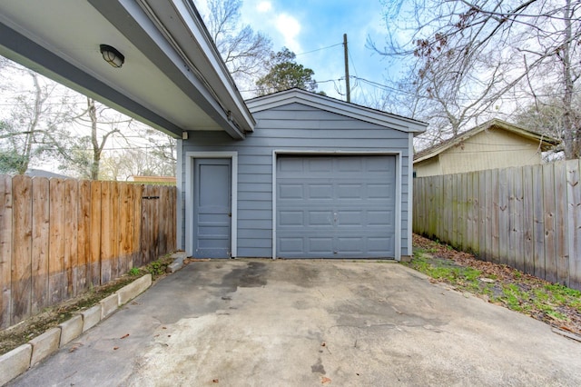 detached garage featuring concrete driveway and fence