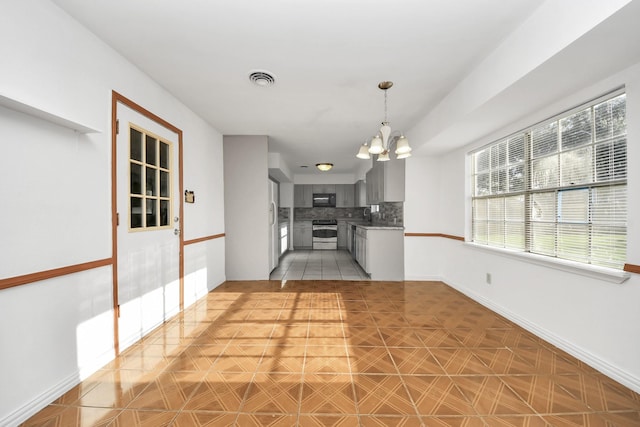 kitchen with light tile patterned flooring, gray cabinetry, stainless steel electric range, a notable chandelier, and backsplash