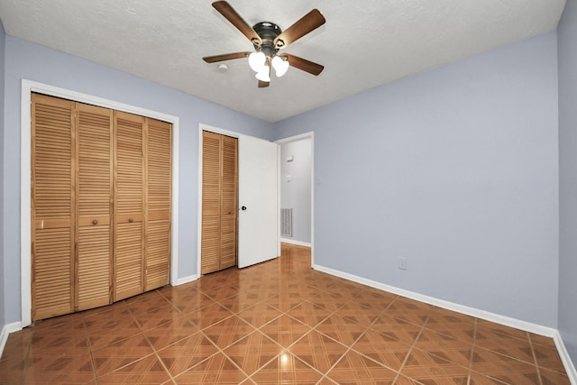 unfurnished bedroom with two closets, a textured ceiling, and ceiling fan