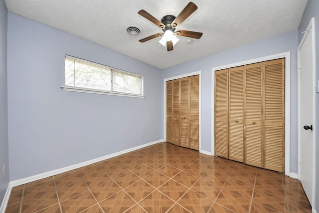 unfurnished bedroom featuring ceiling fan and two closets